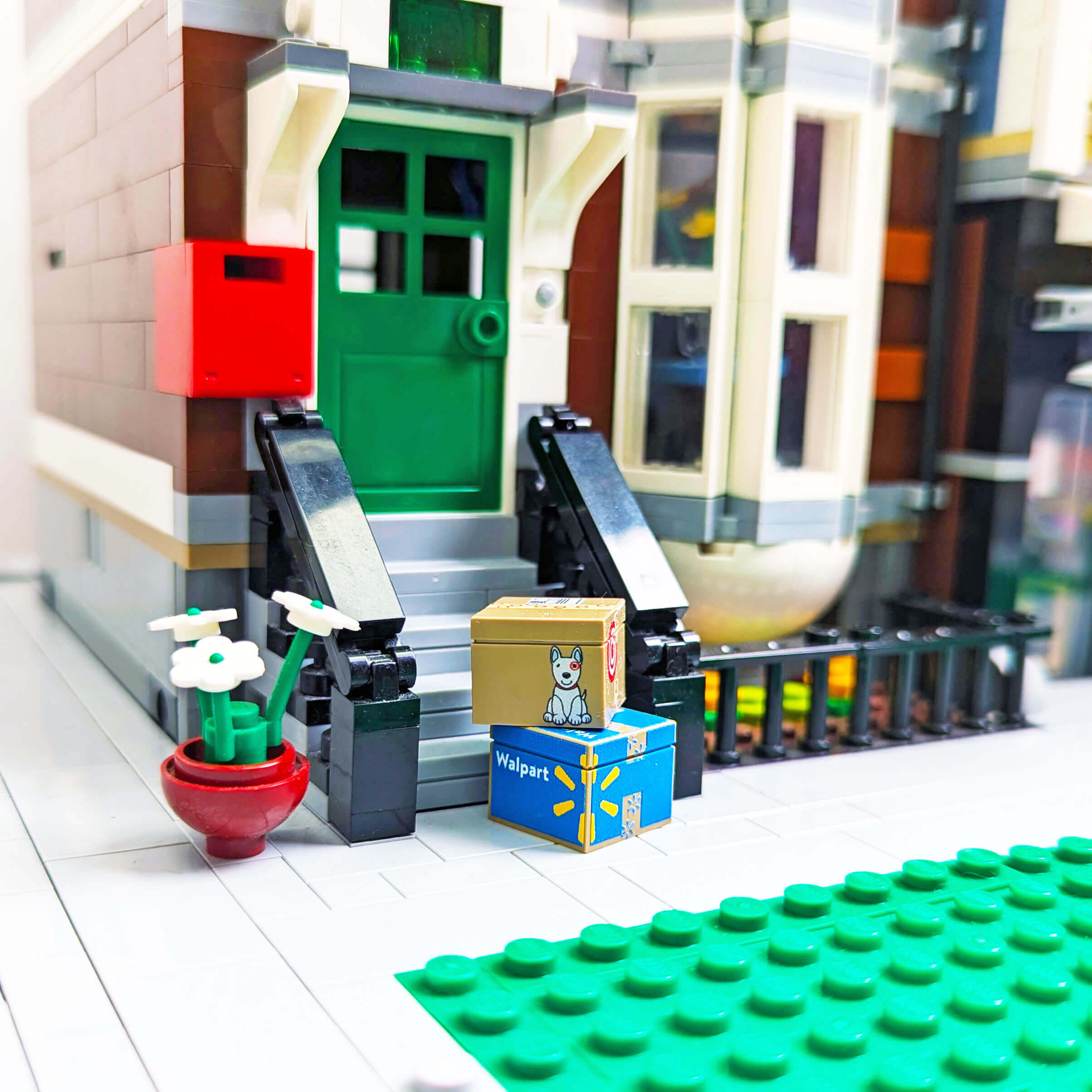 Toy town scene with a green door and a potted plant on a white surface with delivery boxes outside.